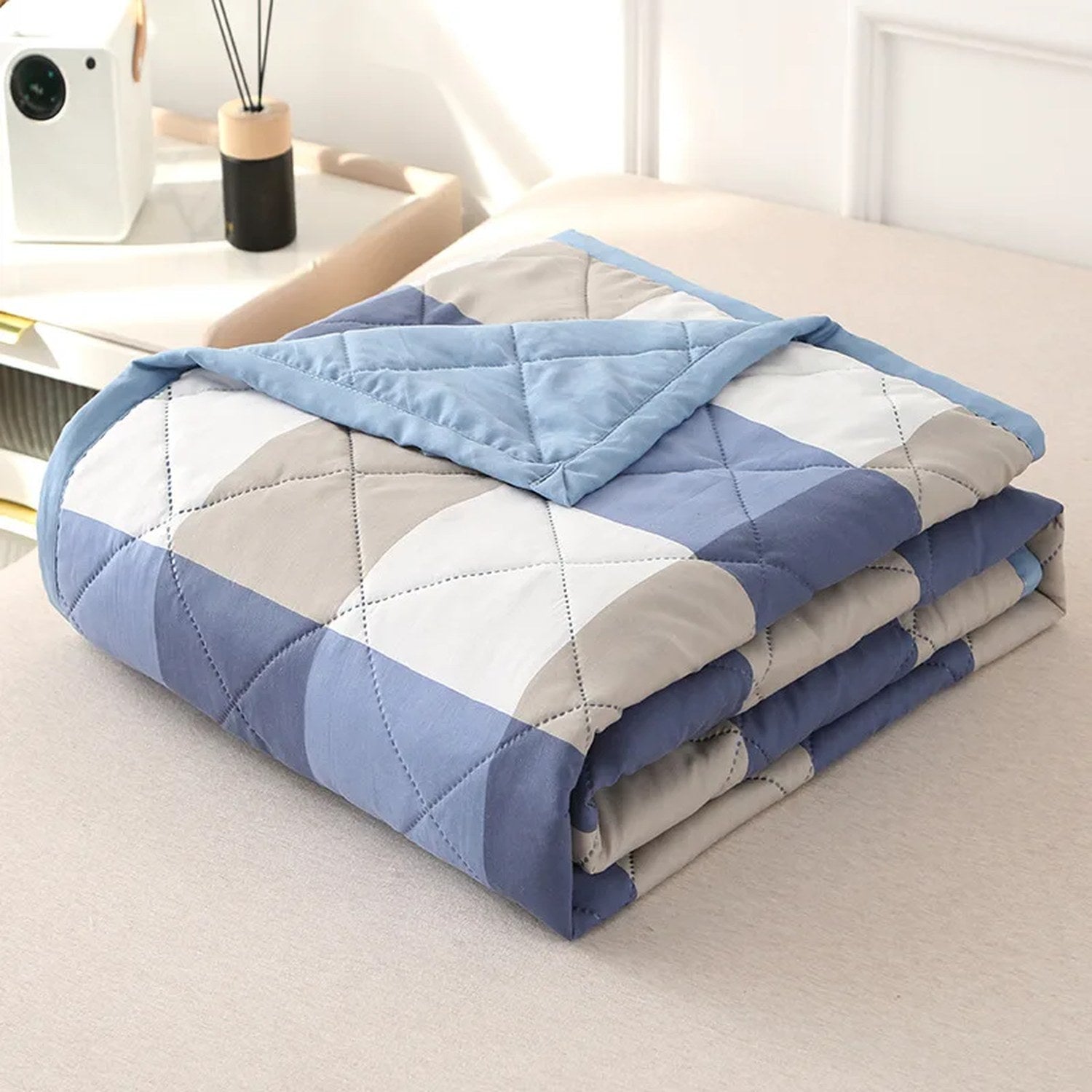 Couette d'été à carreaux bleus et gris pliée montrant le matelassage en losanges