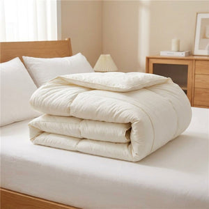 Couette matelassée blanche version mi-saison pliée sur un lit dans une chambre douce