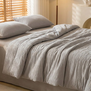 Couette grise en coton seersucker posée sur un grand lit dans une chambre minimaliste