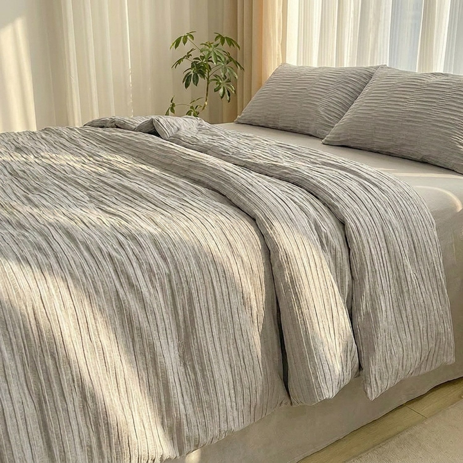 Couette grise en coton seersucker sur un lit dans une chambre lumineuse avec plante verte