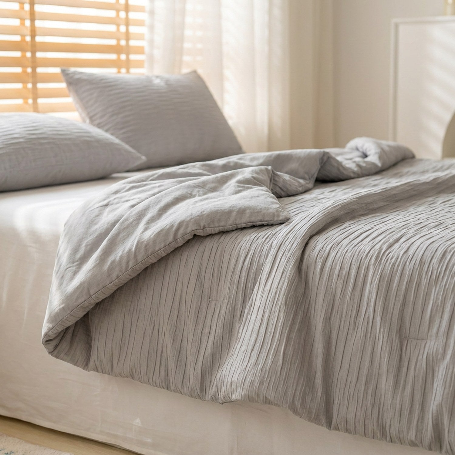 Couette d'été grise en coton seersucker posée sur un lit fait dans une chambre lumineuse