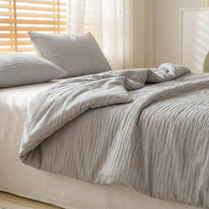 Couette d'été grise en coton seersucker posée sur un lit fait dans une chambre lumineuse