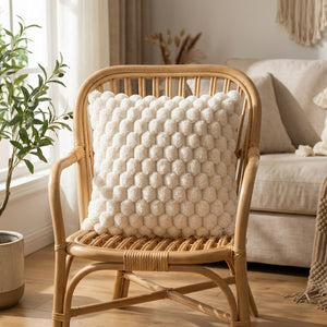 Housse de coussin à pompons crème posée sur un fauteuil en rotin près d'une fenêtre