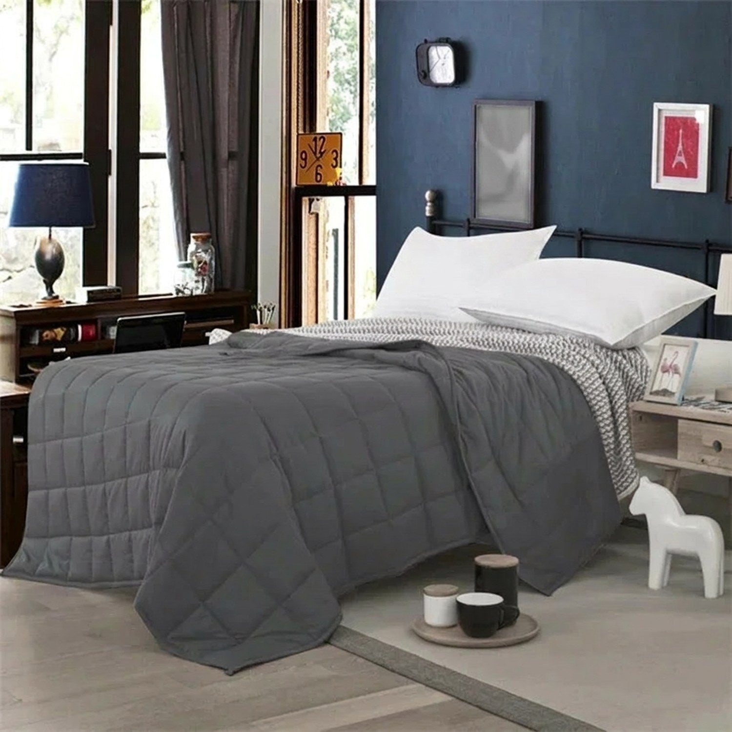 Couverture lestée grise posée sur un lit avec oreillers et tapis