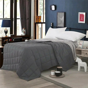 Couverture lestée grise posée sur un lit avec oreillers et tapis