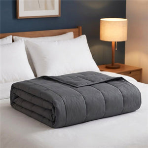 Couverture lestée grise pliée sur un lit avec lampe de chevet allumée