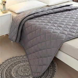 Couverture lestée grise drapée sur un lit avec tapis rond au sol