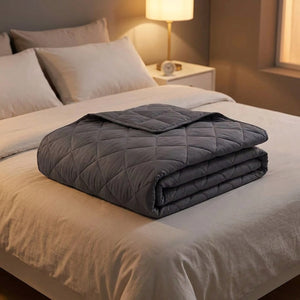 Couverture lestée grise pliée sur un lit avec lampe de chevet allumée