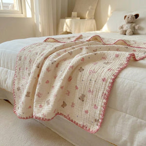 Couverture d'été enfant en gaze de coton à motifs nœuds roses et oursons drapée sur un lit