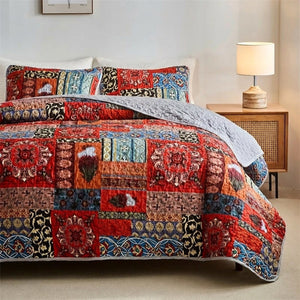Couvre-lit matelassé bohème au patchwork rouge et bleu installé sur un lit dans une chambre lumineuse avec deux taies assorties