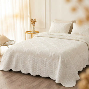 Couvre-lit matelassé blanc à motifs floraux façon boutis posé sur un lit dans une chambre lumineuse