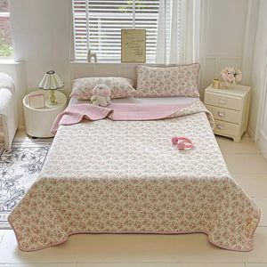 Couvre-lit matelassé imprimé floral rose sur un lit avec liseuse et bougeoir sur la table de chevet