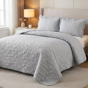 Couvre-lit matelassé gris avec deux taies assorties sur un lit dans une chambre lumineuse