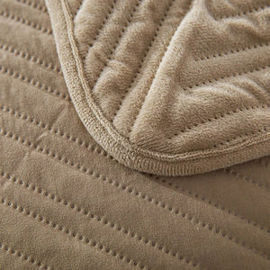 Gros plan sur la texture velours et le piqué géométrique du couvre-lit