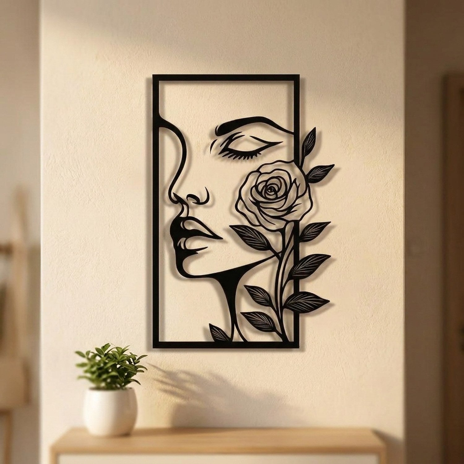 Décoration murale en métal noir représentant un visage de femme et une rose accrochée à un mur clair