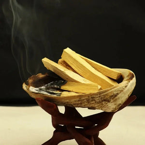Bâtons d'encens Palo Santo dans un bol coquillage sur support bois avec fumée