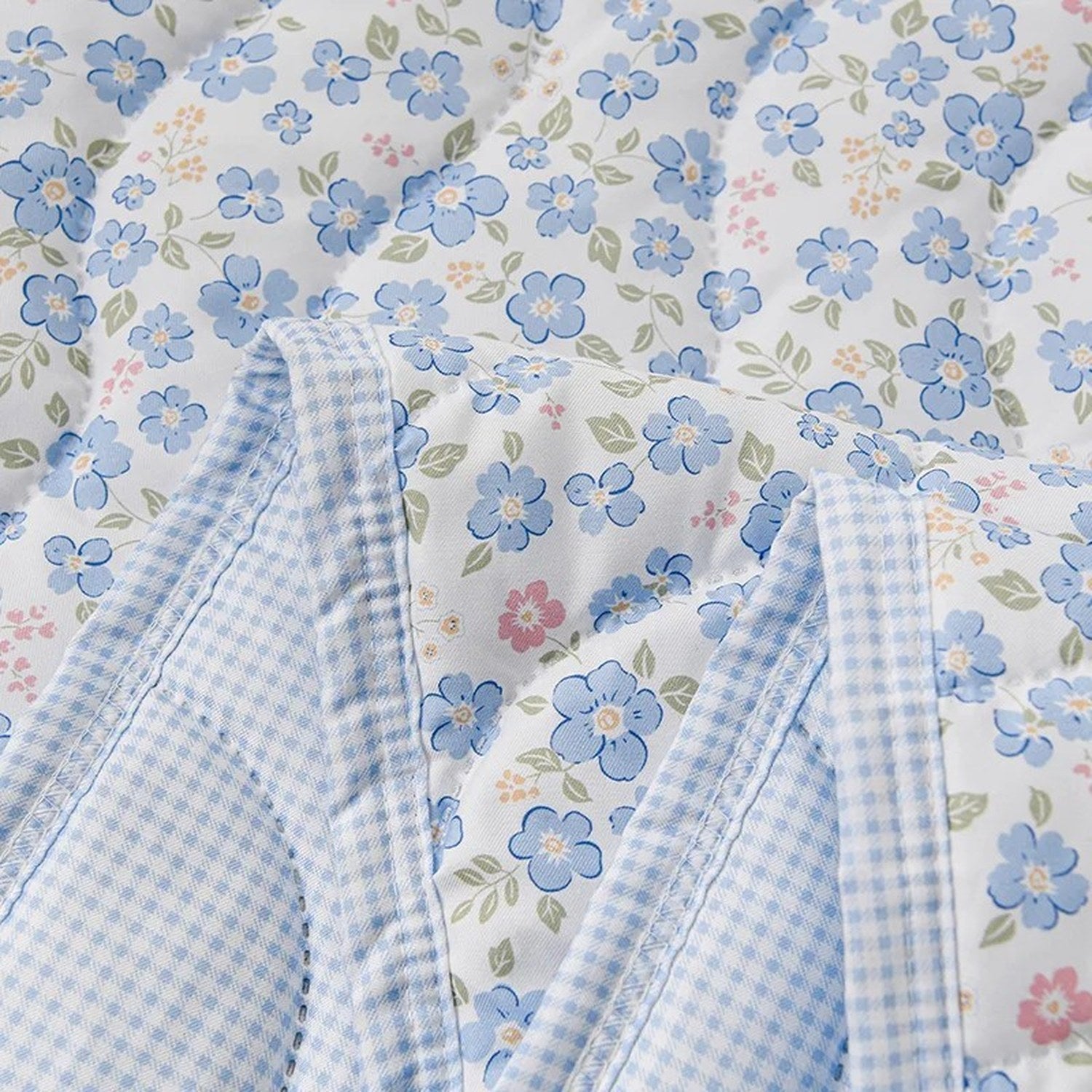 Détail du tissu matelassé de la couette d'été à fleurs bleues et de son envers à carreaux vichy