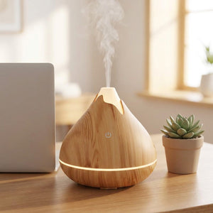 Diffuseur ultrasonique en bois clair diffusant une brume sur un bureau à côté d'un ordinateur portable