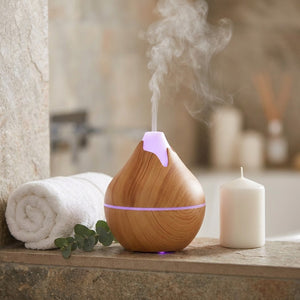 Diffuseur ultrasonique en bois clair avec lumière LED violette sur une étagère de salle de bain