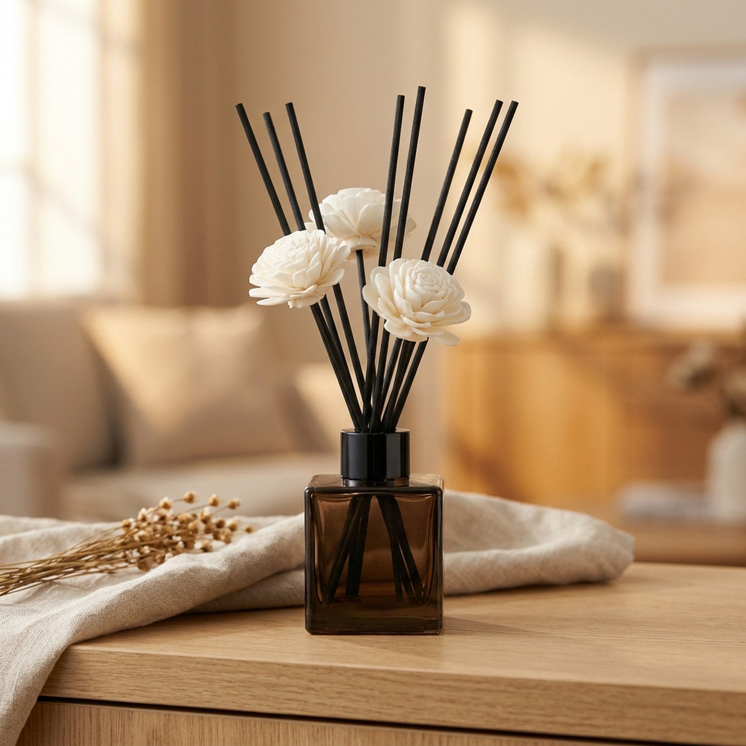 Diffuseur à bâtonnets en flacon de verre teinté avec fleur blanche et tiges noires sur une console claire