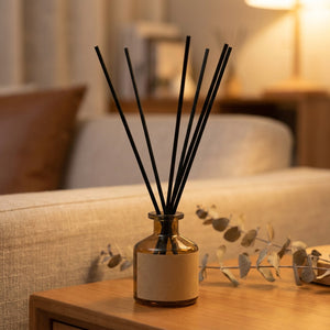 Diffuseur de parfum à bâtonnets dans un flacon en verre ambré posé sur une table en bois