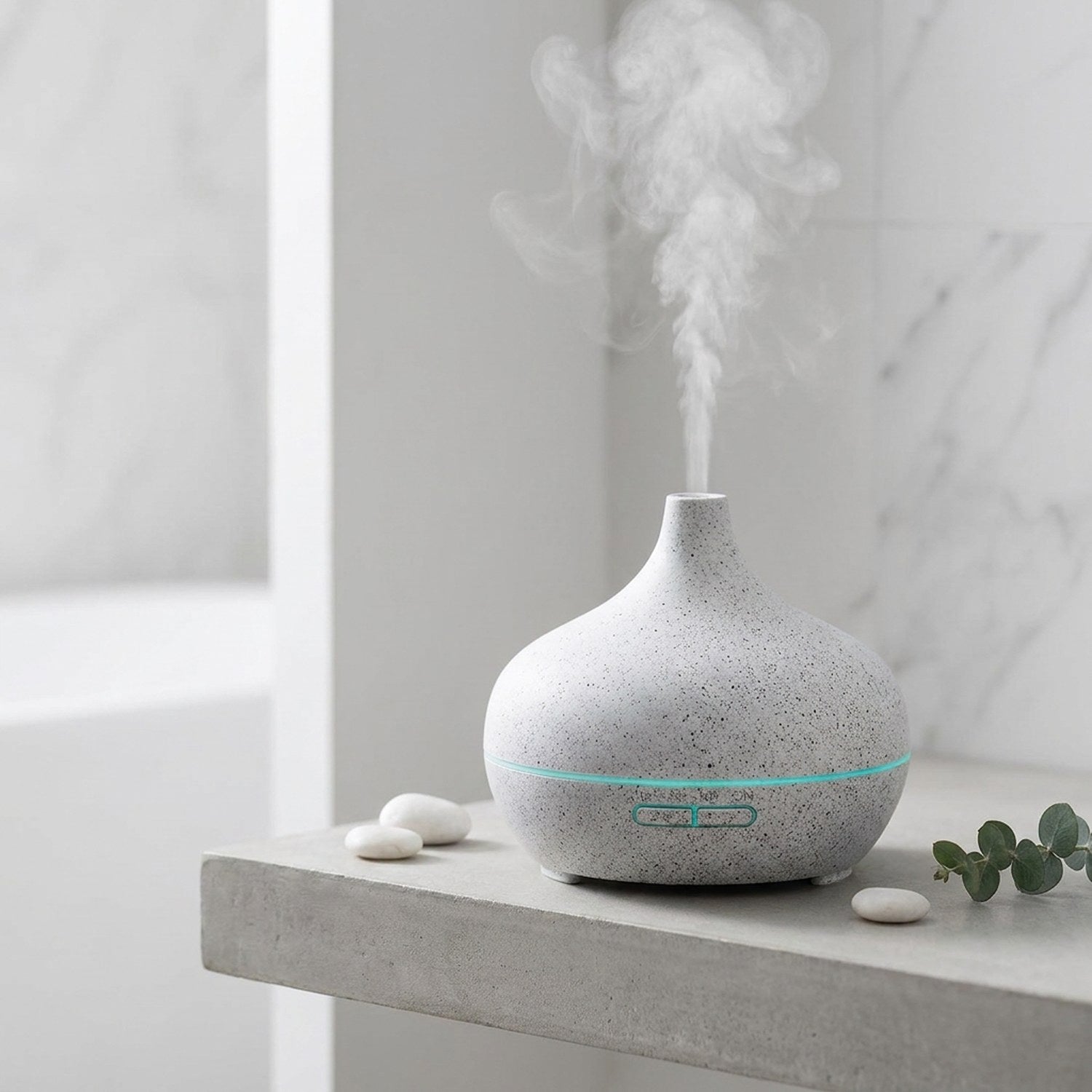Diffuseur d'arômes motif marbre blanc sur étagère béton, pebbles blancs et eucalyptus, ambiance spa