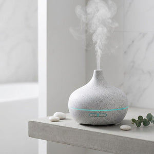 Diffuseur d'arômes motif marbre blanc sur étagère béton, pebbles blancs et eucalyptus, ambiance spa