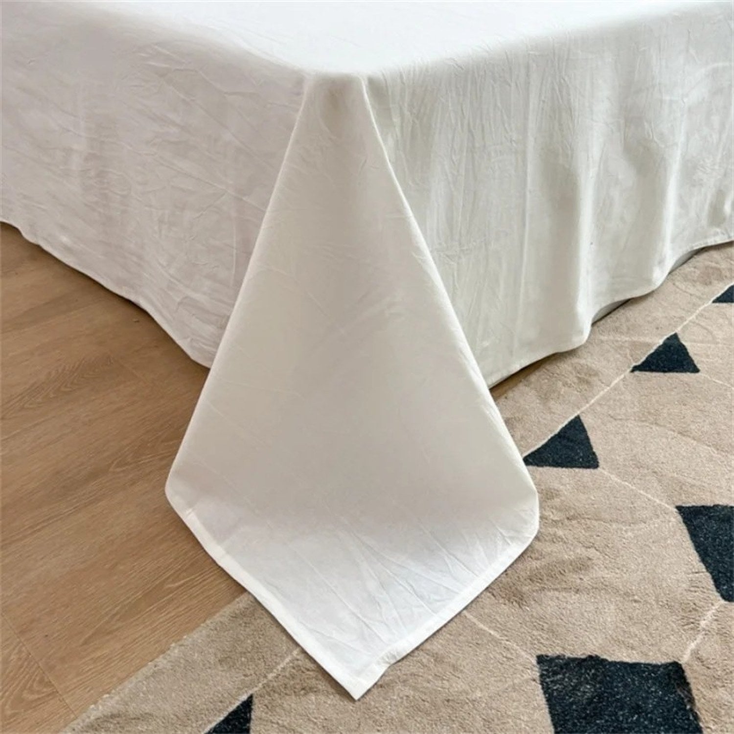 Coin du drap plat en coton drapé sur le matelas avec tissu qui retombe au sol