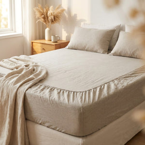 Drap-housse en lin lavé naturel posé sur un lit fait dans une chambre lumineuse et chaleureuse