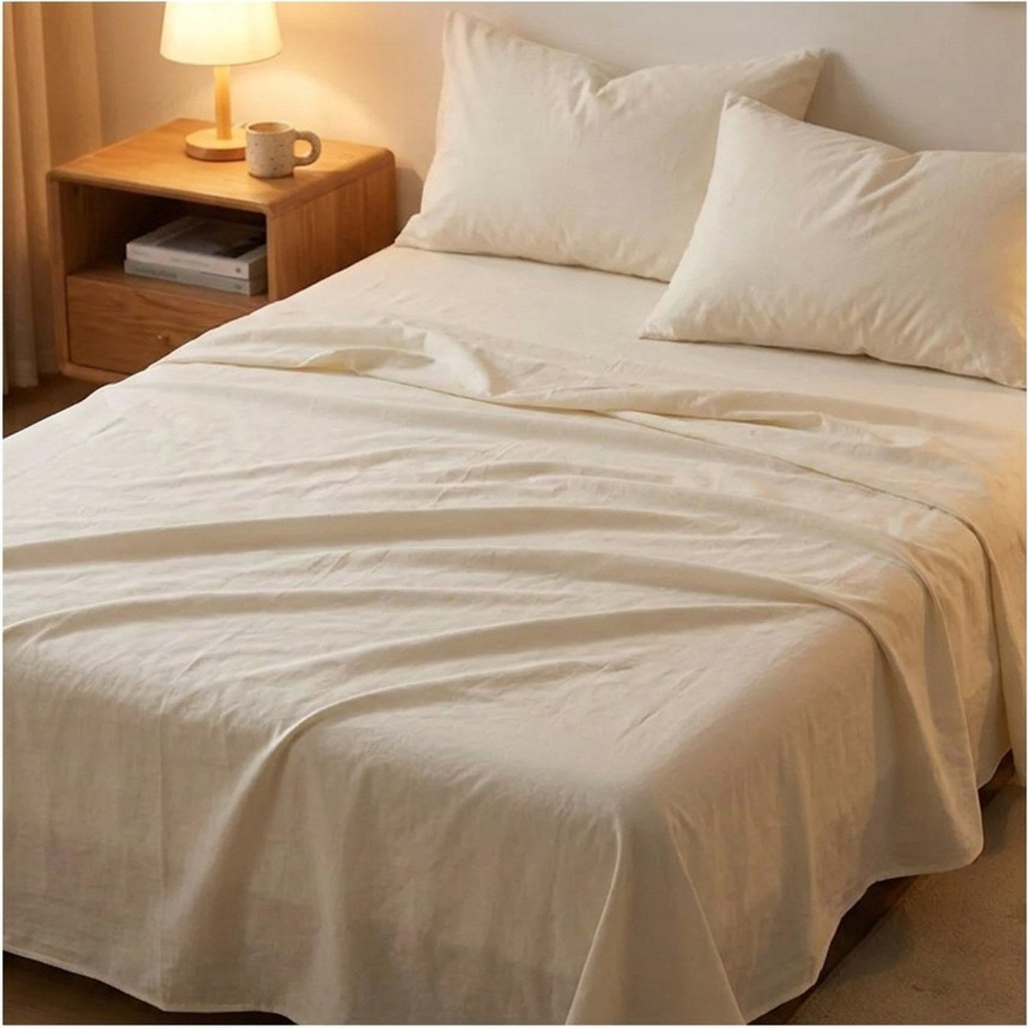 Drap plat en coton crème sur un lit avec table de chevet en bois et lampe allumée