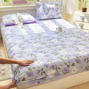Drap-housse en coton à grandes fleurs mauves installé sur un lit avec deux taies assorties