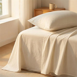 Drap plat en coton crème posé sur un lit fait avec oreiller dans une chambre lumineuse