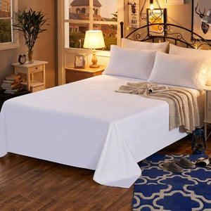 Drap plat blanc en coton sur un lit dans une chambre chaleureuse avec lampe de chevet allumée