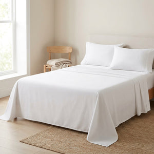 Drap plat blanc en coton fait sur un lit dans une chambre épurée avec chaise en bois