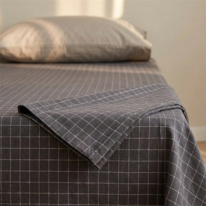 Drap plat en coton gris à carreaux plié en pointe sur un lit avec oreiller