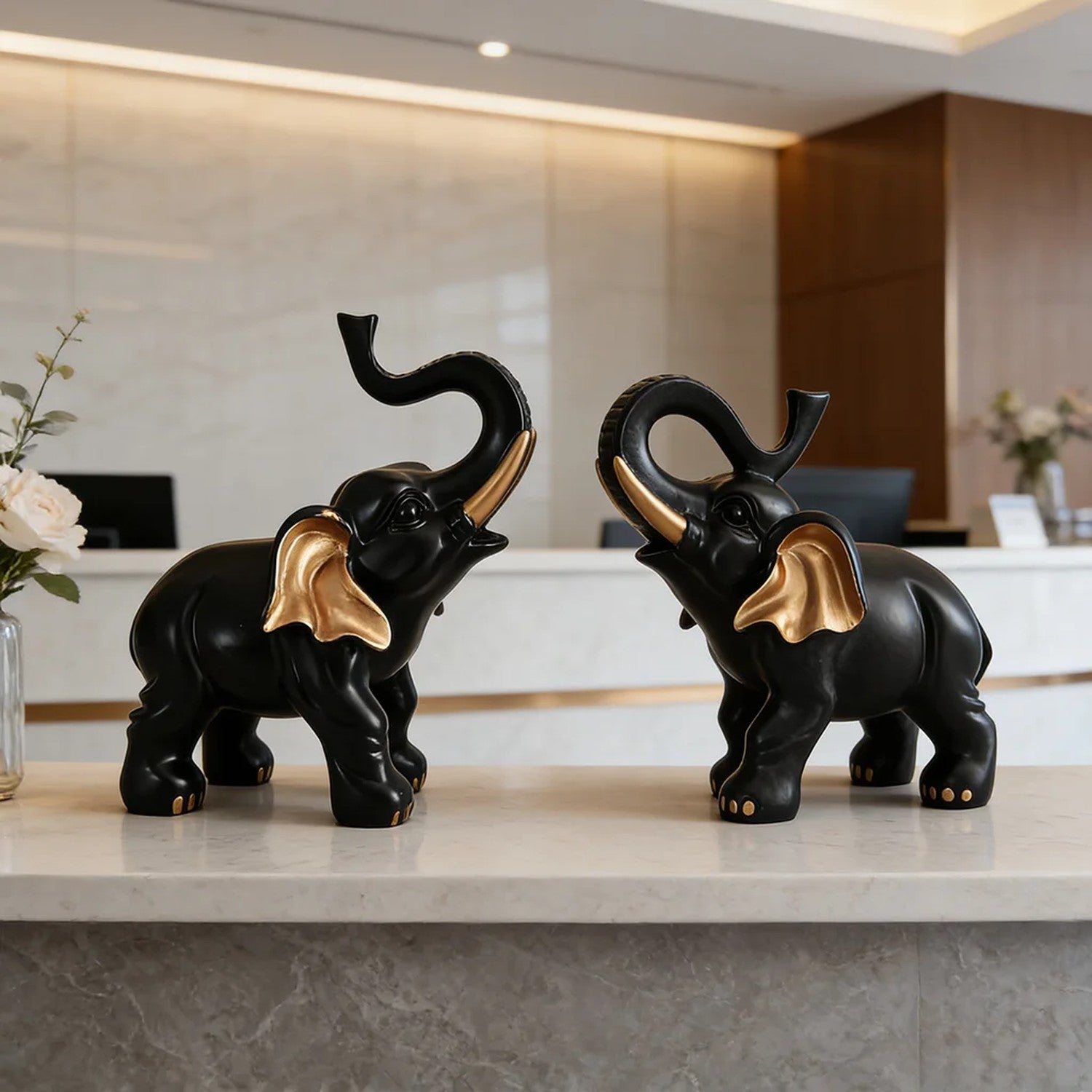 Deux figurines éléphant noir et or trompe levée sur comptoir en marbre blanc