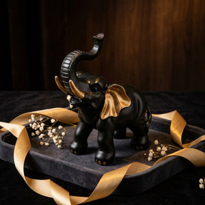Figurine éléphant en résine noire et or présentée comme cadeau sur plateau de velours sombre avec rubans dorés