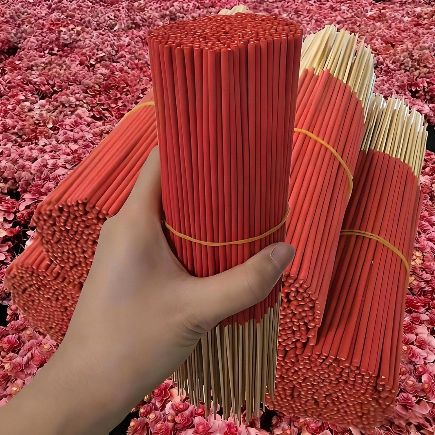Grands lots de bâtonnets d'encens sang de dragon rouge tenus à la main sur fond de fleurs roses
