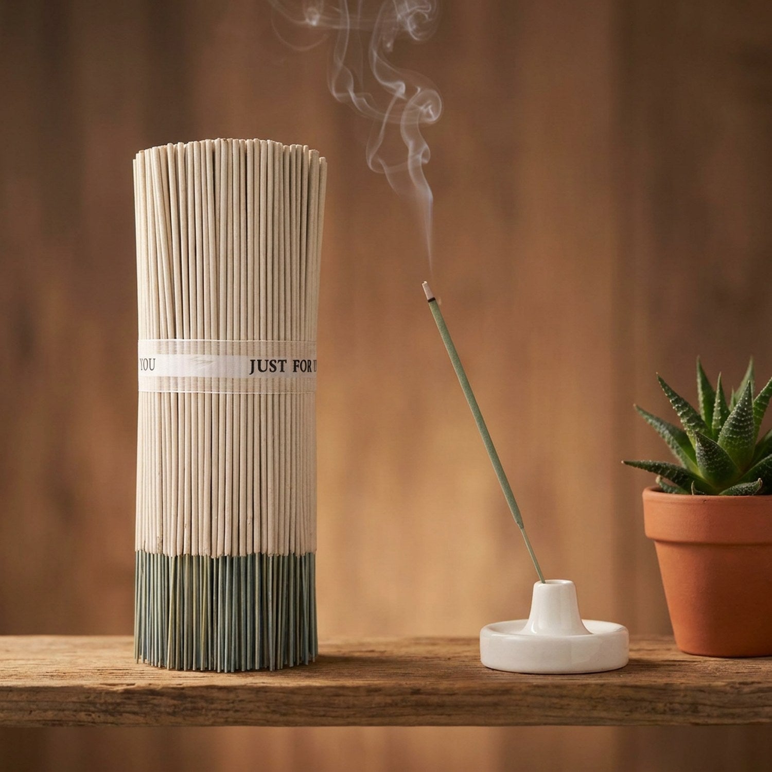Bâtonnets d'encens sauge artisanaux en fagot avec bâtonnet allumé dans un porte-encens céramique sur une planche en bois