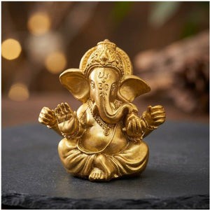 Figurine Ganesha dorée en résine posée sur une ardoise sombre avec bokeh chaleureux