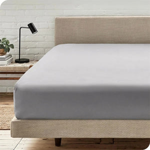 Drap-housse gris installé sur un lit dans une chambre lumineuse