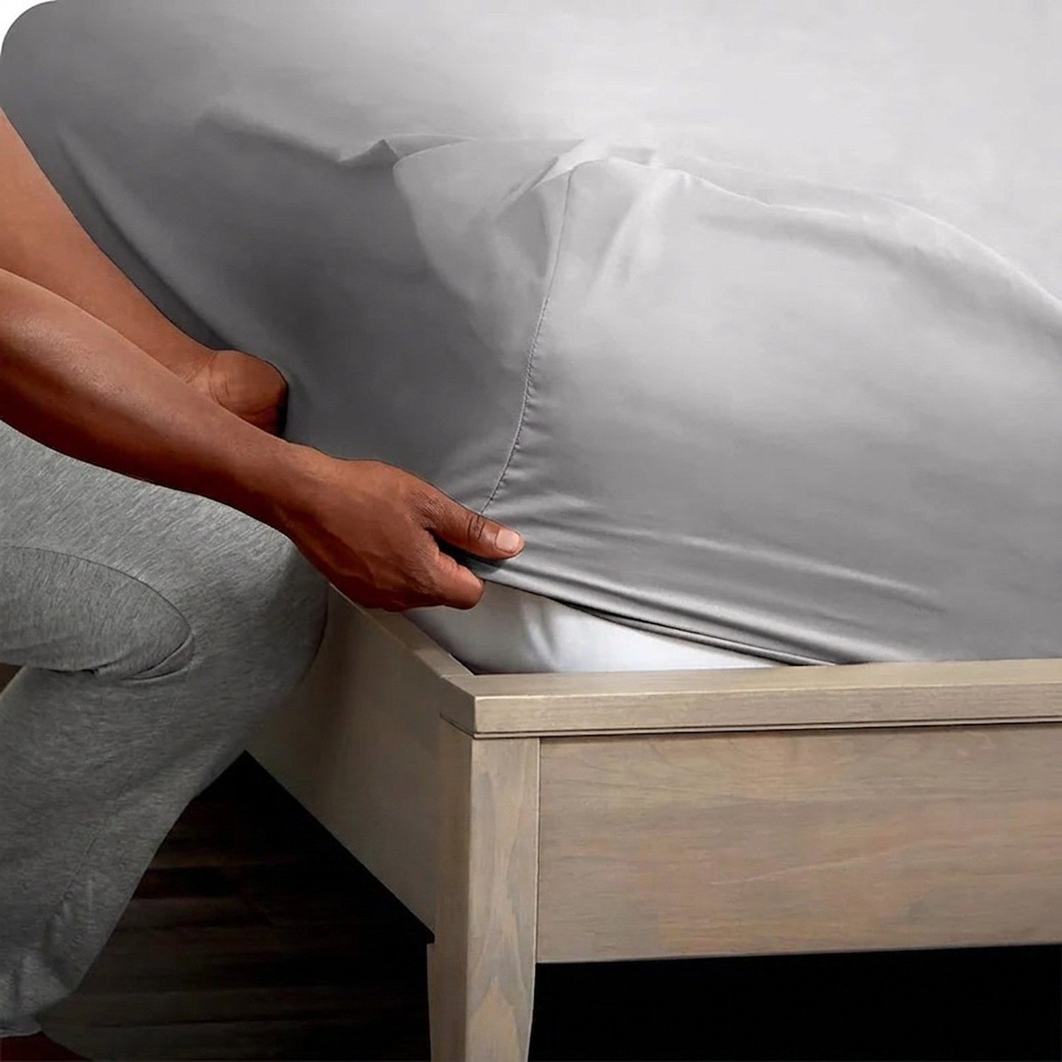 Main ajustant le drap-housse gris sur le coin d'un matelas