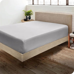 Drap-housse gris sur un lit dans une chambre cosy avec une plante verte