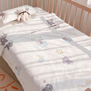 Parure de lit bébé motif éléphant étoilé installée sur un lit à barreaux avec un nounours