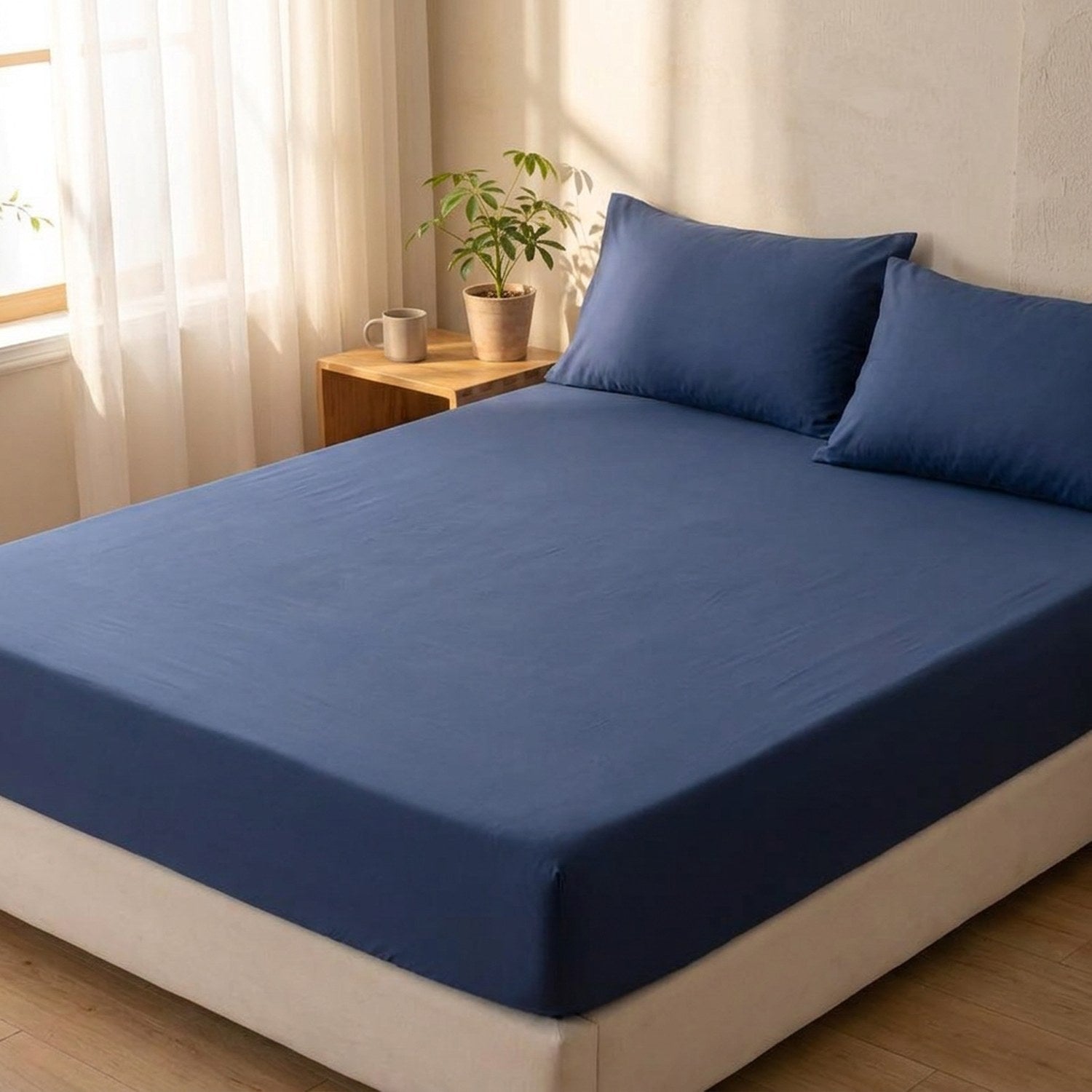 Drap-housse bleu marine installé sur un lit dans une chambre lumineuse avec table de chevet en bois