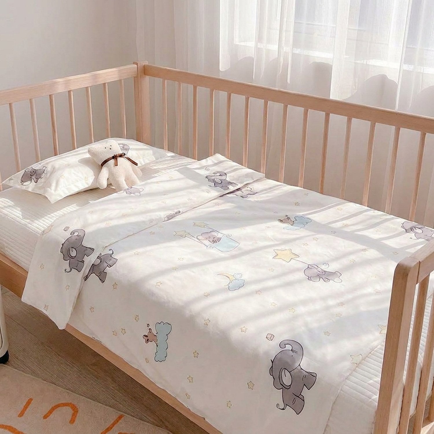 Parure de lit bébé en coton blanc cassé avec motif éléphant étoilé installée sur un lit à barreaux dans une chambre lumineuse