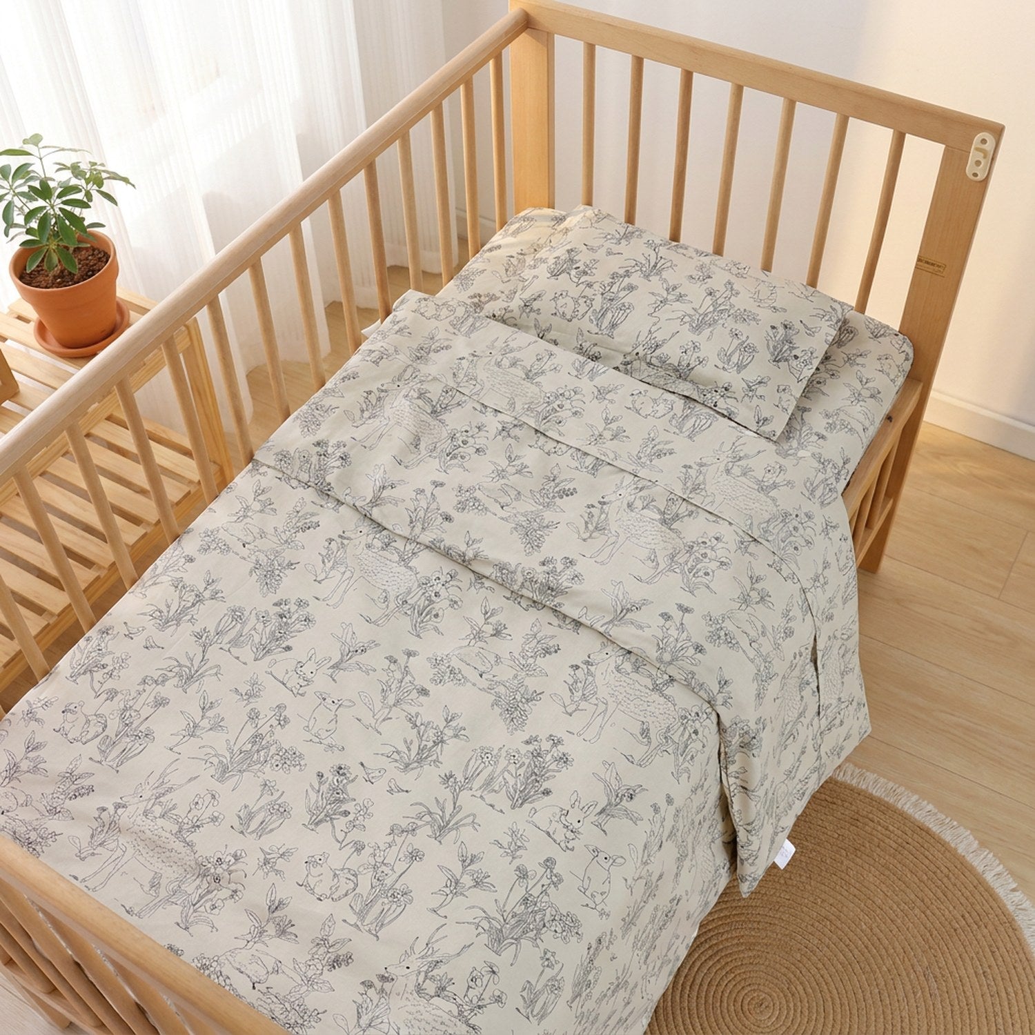 Parure de lit bébé au motif nature dessiné à la main installée sur un lit à barreaux près d'une fenêtre
