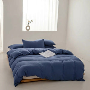 Parure de lit unie bleu foncé avec housse de couette et taies posée sur un lit dans une chambre lumineuse et épurée