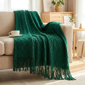 Couverture tricotée vert foncé à franges en maille losange sur un canapé