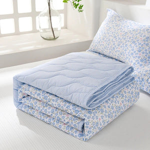 Couette d'été bleue à fleurs pliée sur un lit avec une taie d'oreiller assortie